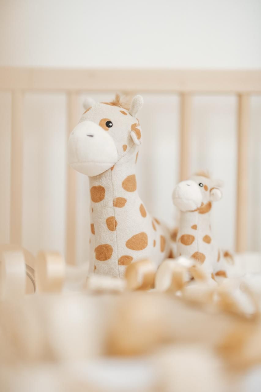 Decorative plush giraffe toys lined up in a soft focus nursery setting with beige and white tones.