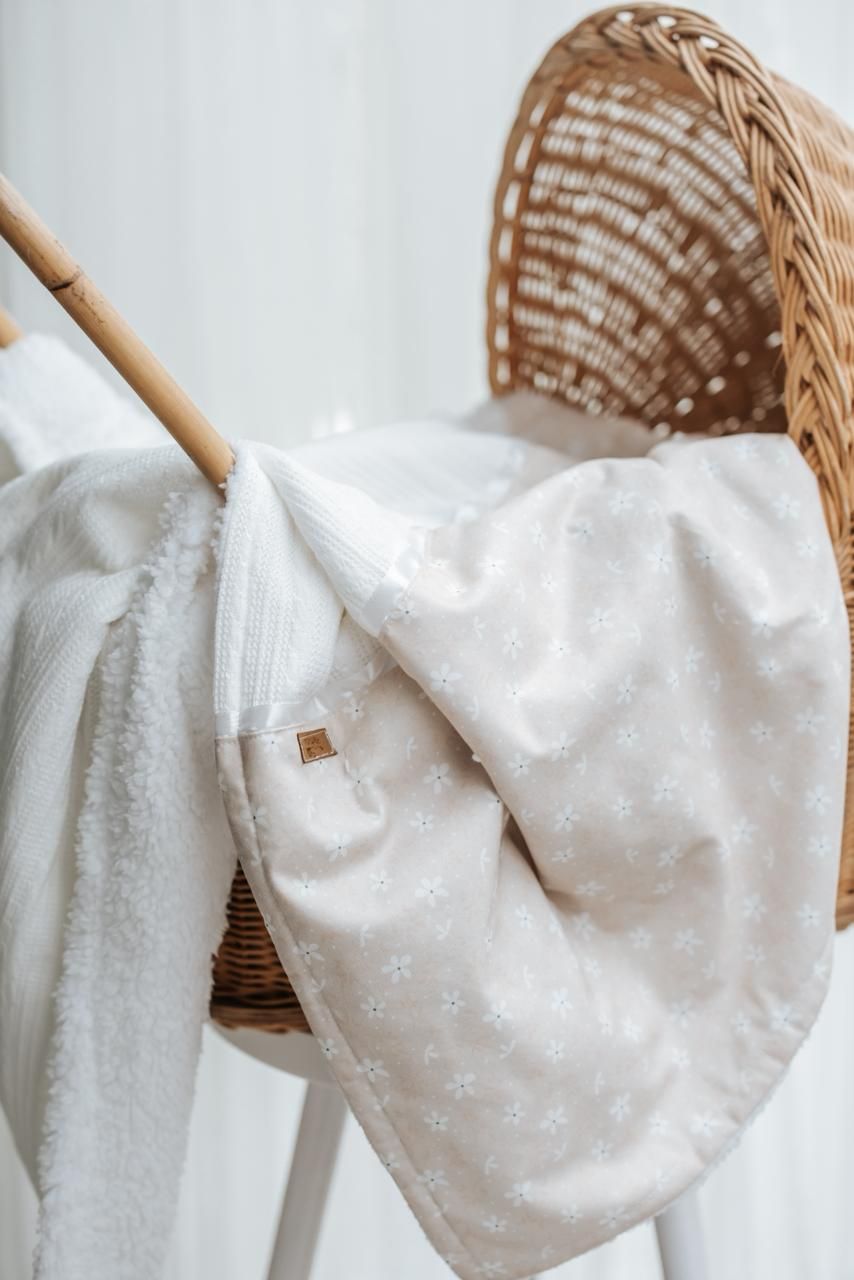 White baby blanket with delicate star pattern draped over woven wicker basket showing soft texture and gentle folds.