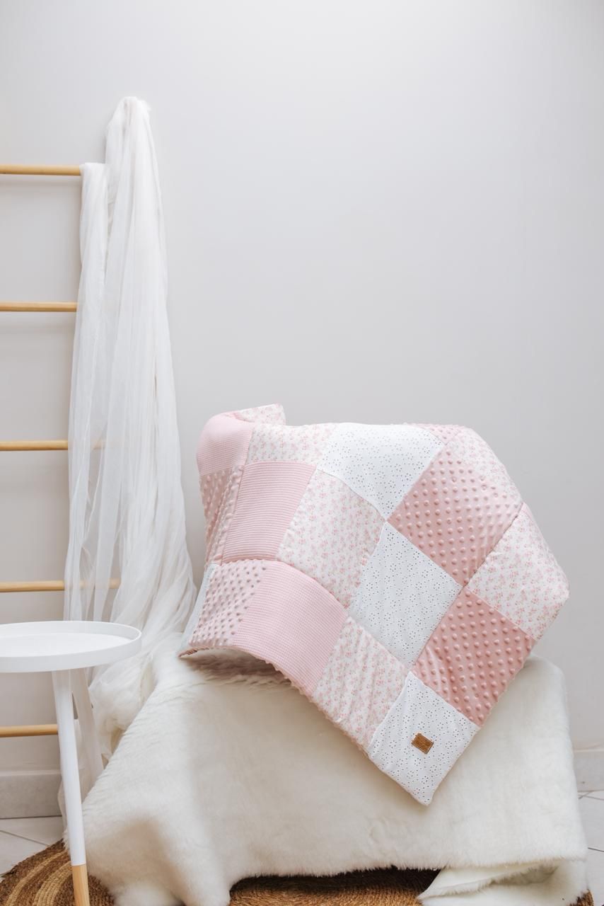 Pink and white patchwork pillows with polka dot pattern arranged on white bedding with flowing sheer curtains.