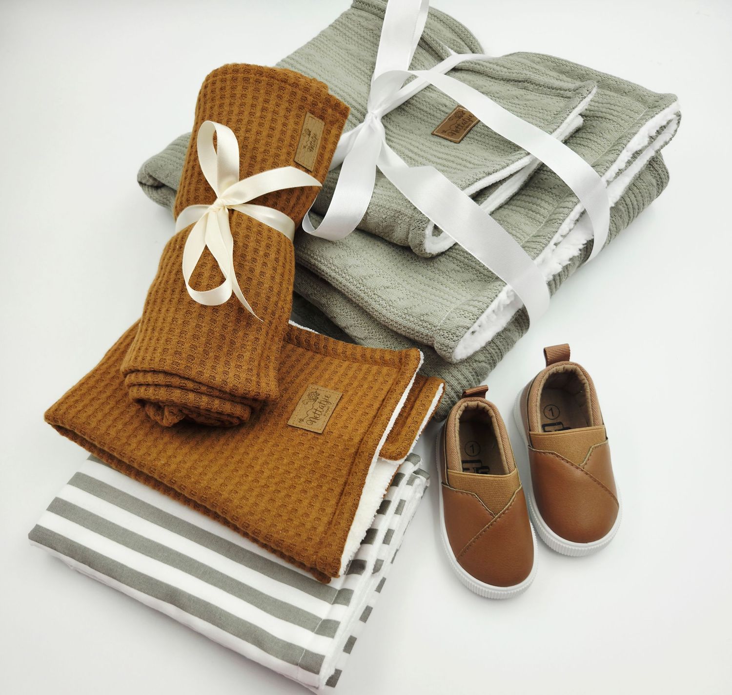 Folded baby blankets in brown and gray with leather shoes and white ribbons.