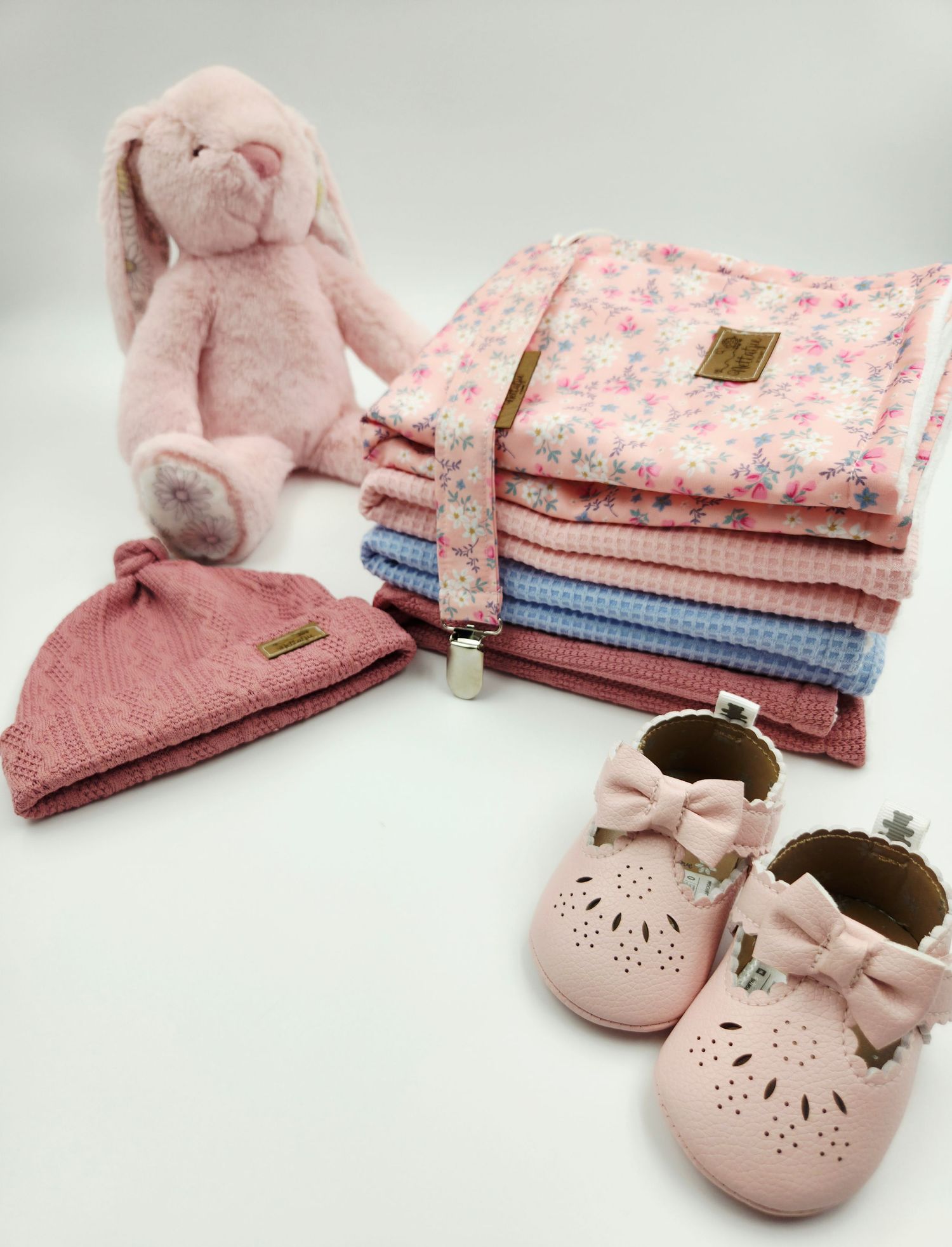 Pink plush bunny with stacked floral and textured blankets and pink bow shoes.