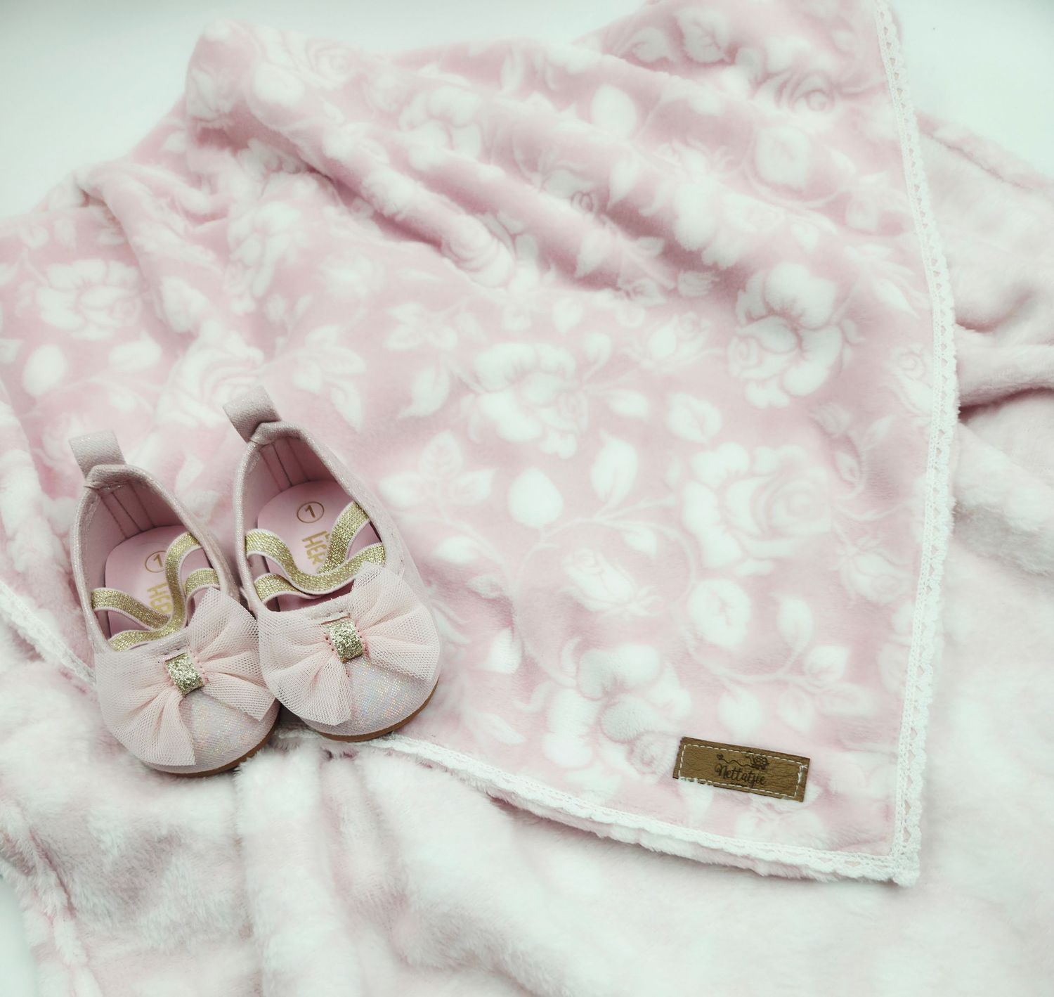 Pink textured baby blanket with matching bow shoes on white background.