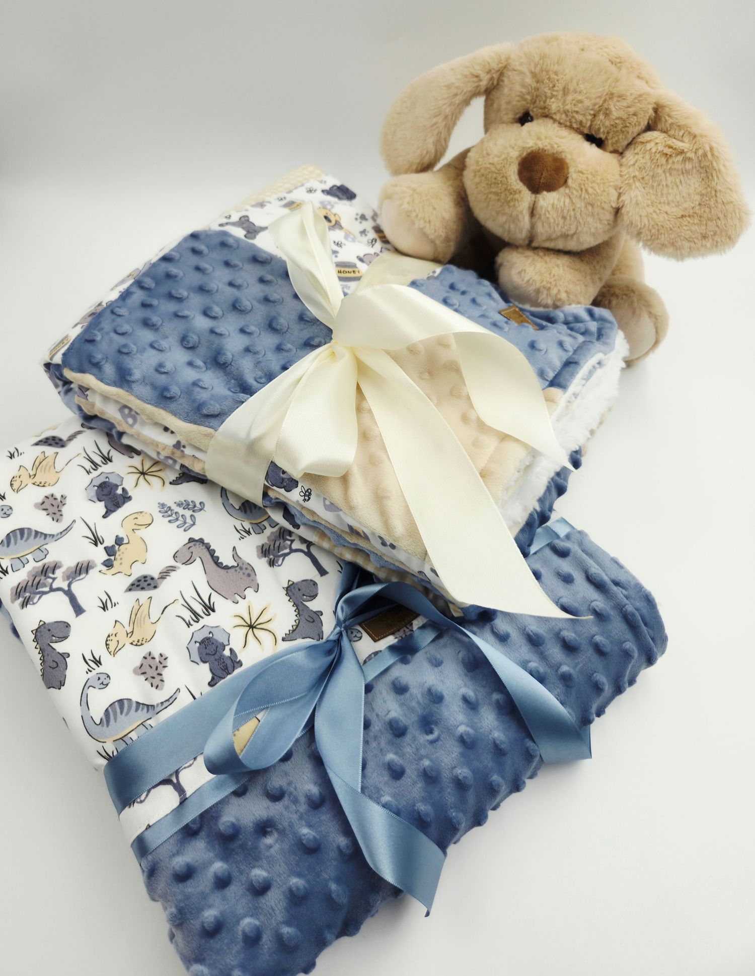 Plush puppy toy displayed on folded patchwork blanket with white satin bow.