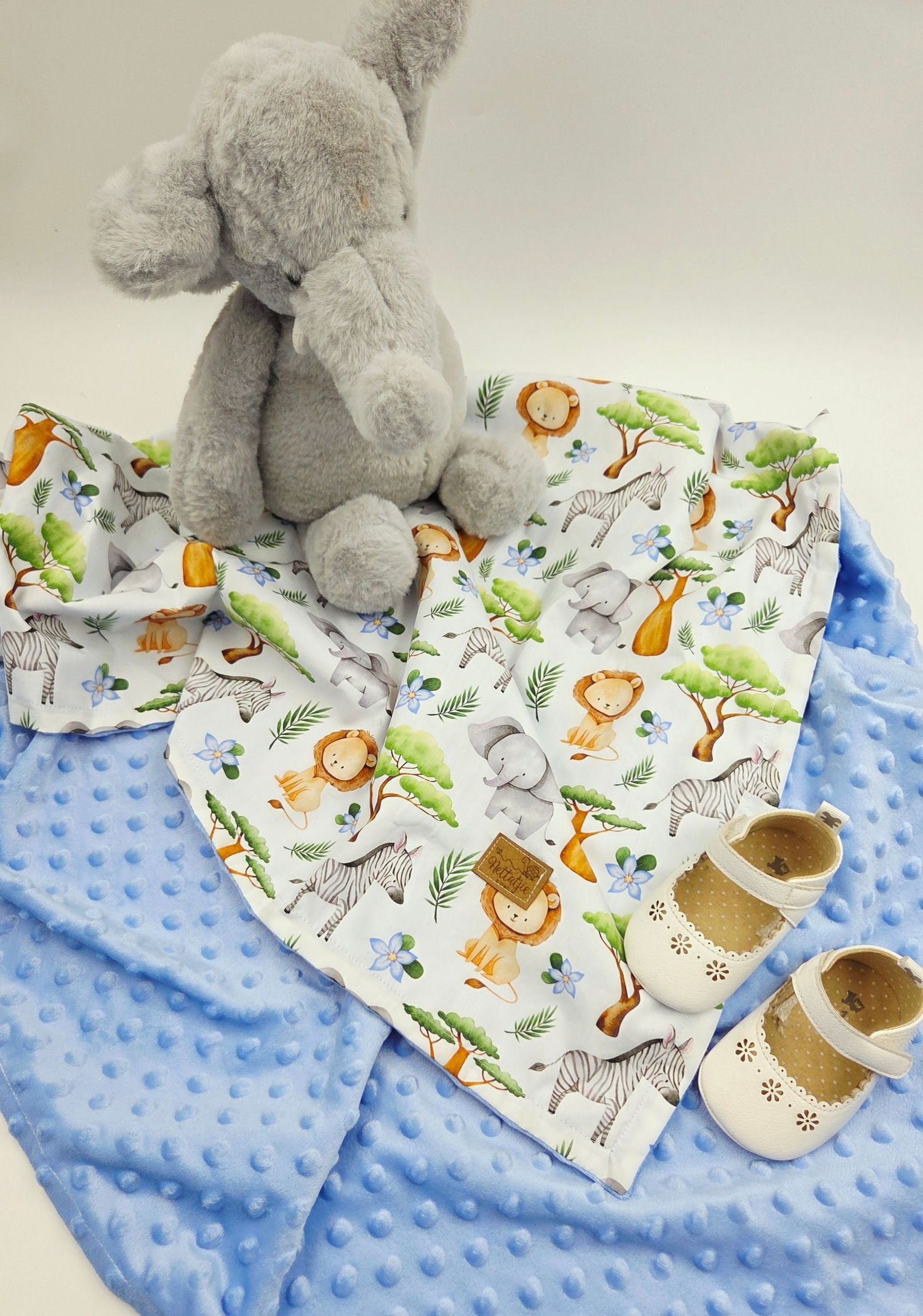Grey stuffed elephant on safari print baby blanket with blue minky fabric and tan shoes.