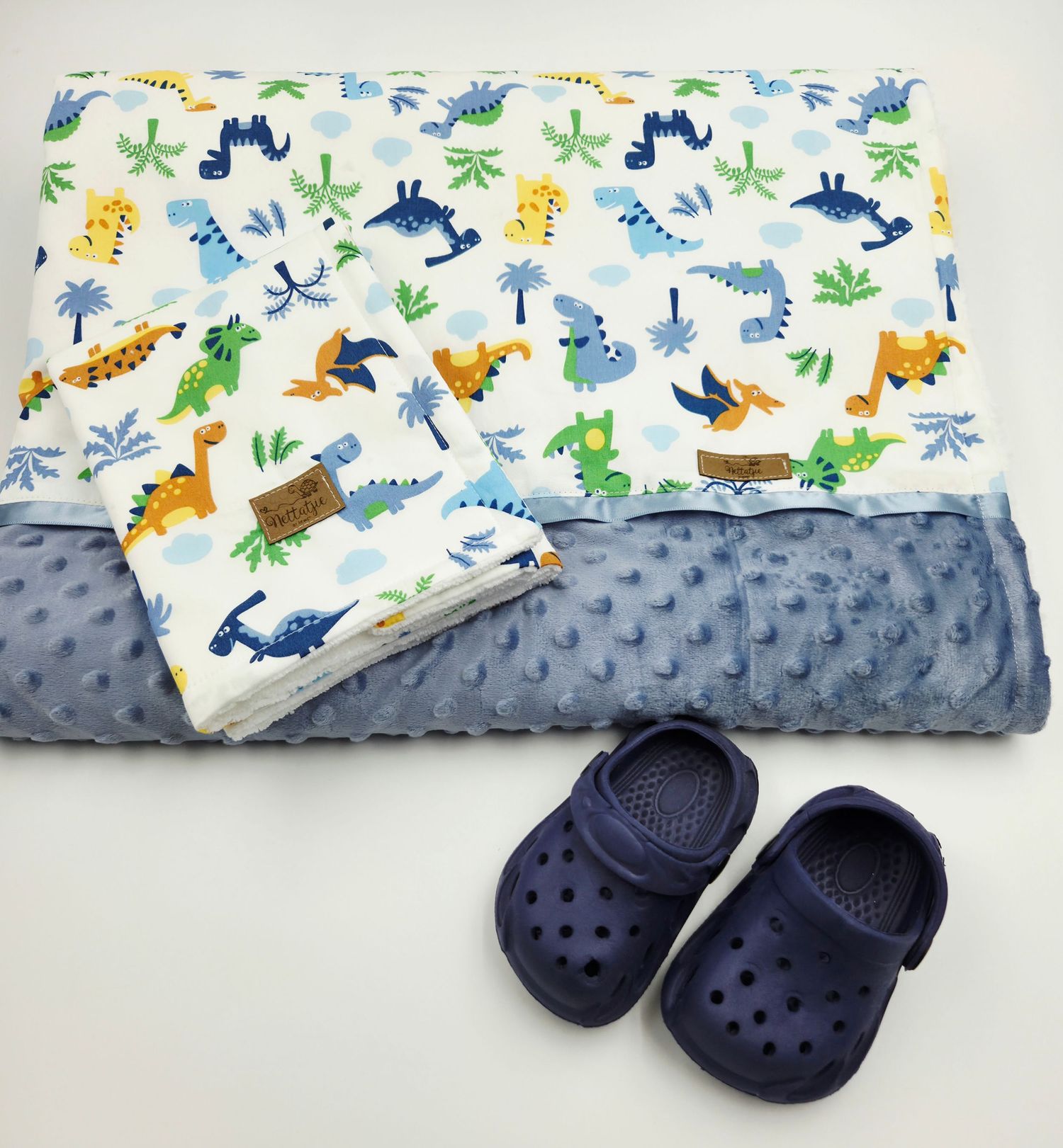Dinosaur print baby blanket paired with navy blue crocs shoes.