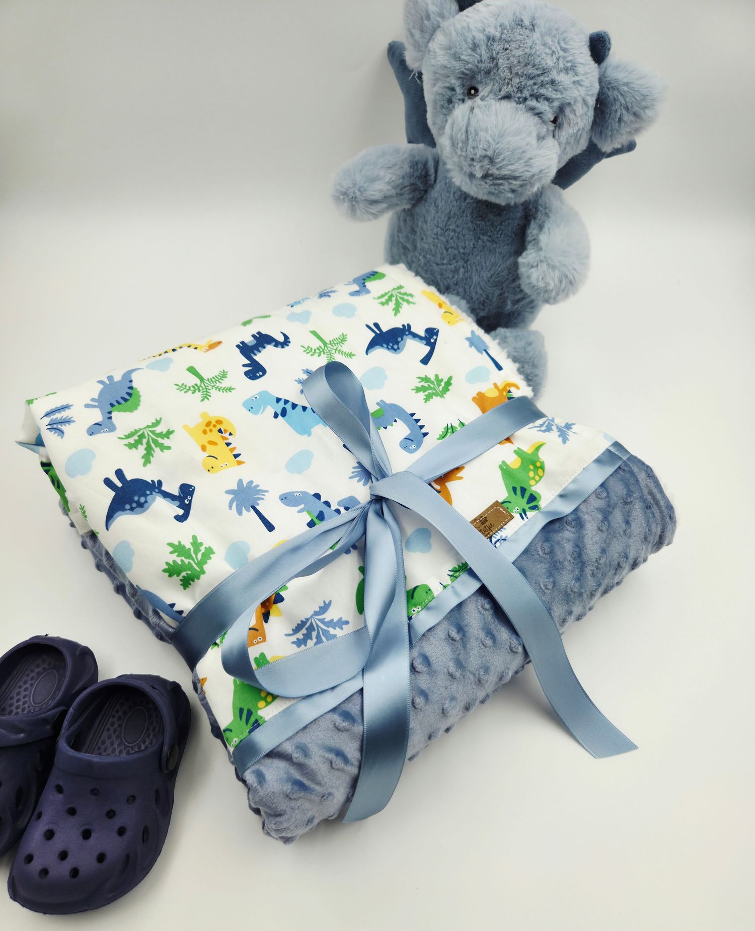 Soft gray minky blanket with dinosaur print fabric and navy blue Crocs shoes arranged on white background.