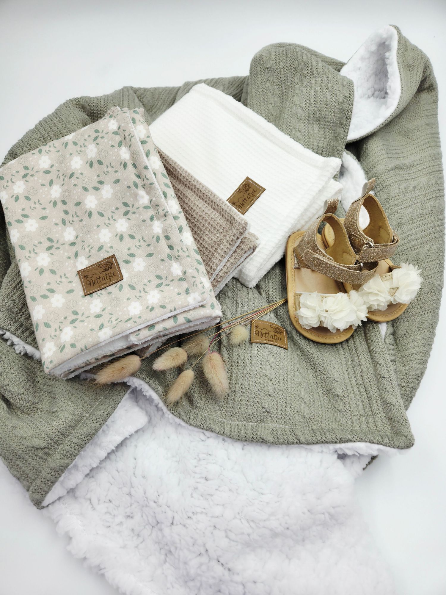 Sage green knit blanket with floral print fabric and gold sandals arranged on white surface.