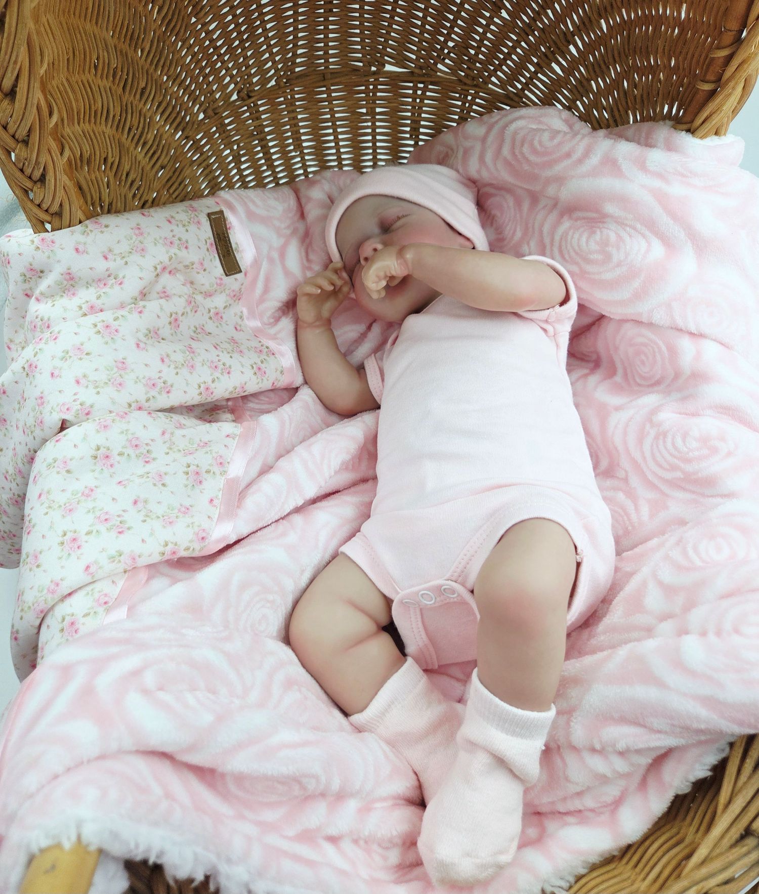 Baby resting on soft pink floral bedding in a wicker bassinet.
