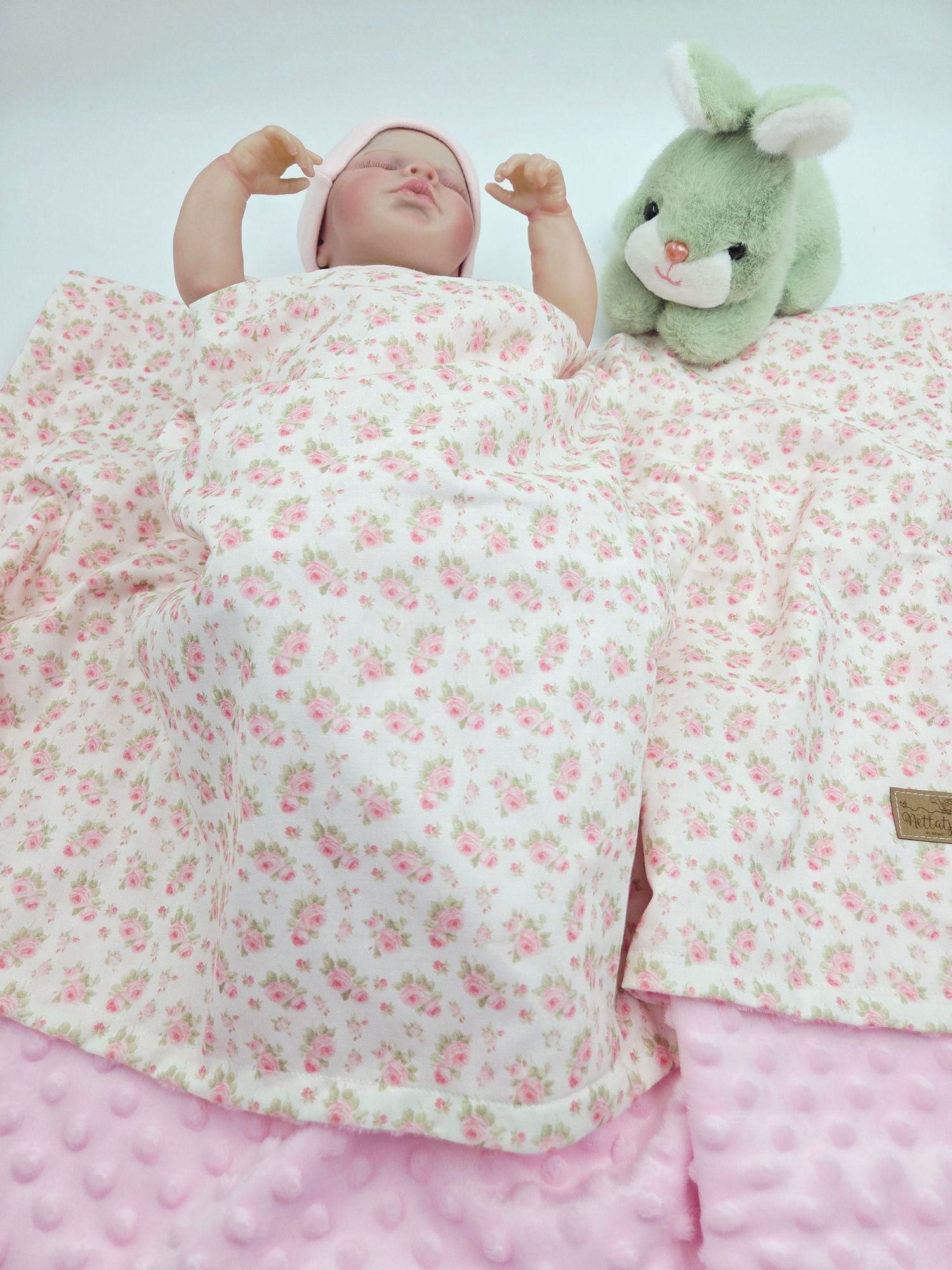 Baby blanket with floral pattern and green plush bunny on textured pink fabric.