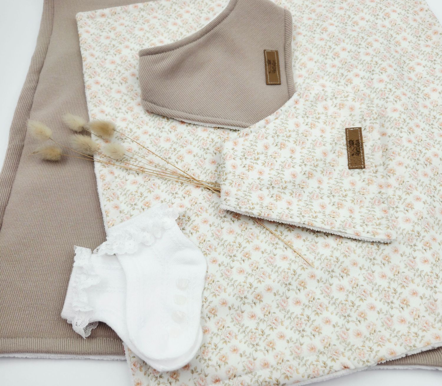 White and beige baby clothing items with floral patterns laid out on a light background.