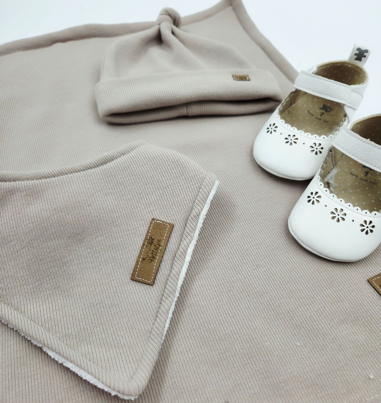 Beige baby clothing and white shoes displayed with leather tags and delicate details.
