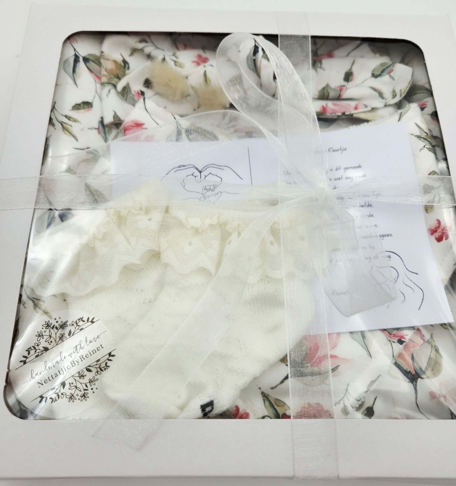 Neatly folded baby clothing with floral prints and handwritten notes in a presentation box.