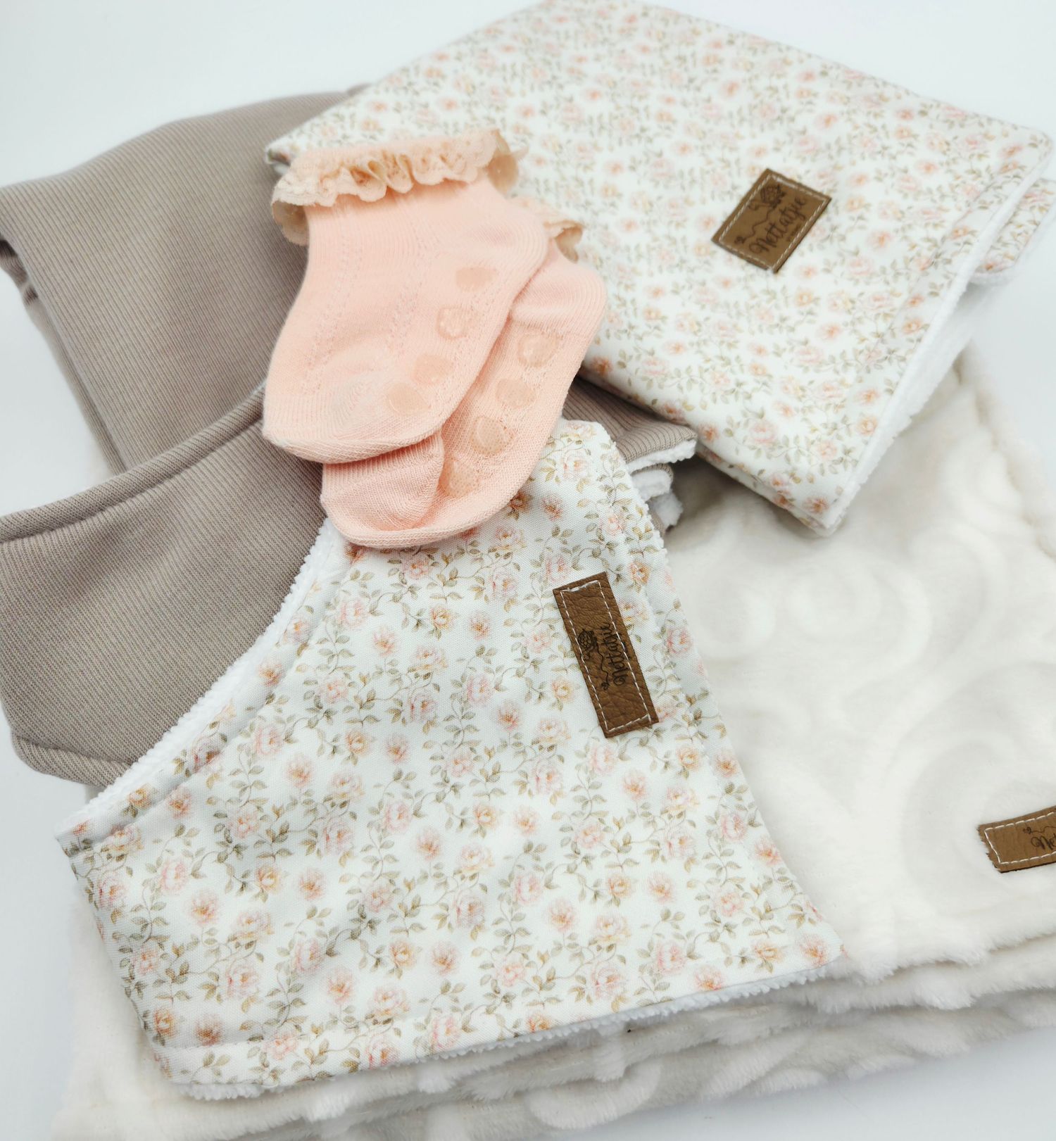 Floral print baby blanket with peach mittens and white accents.