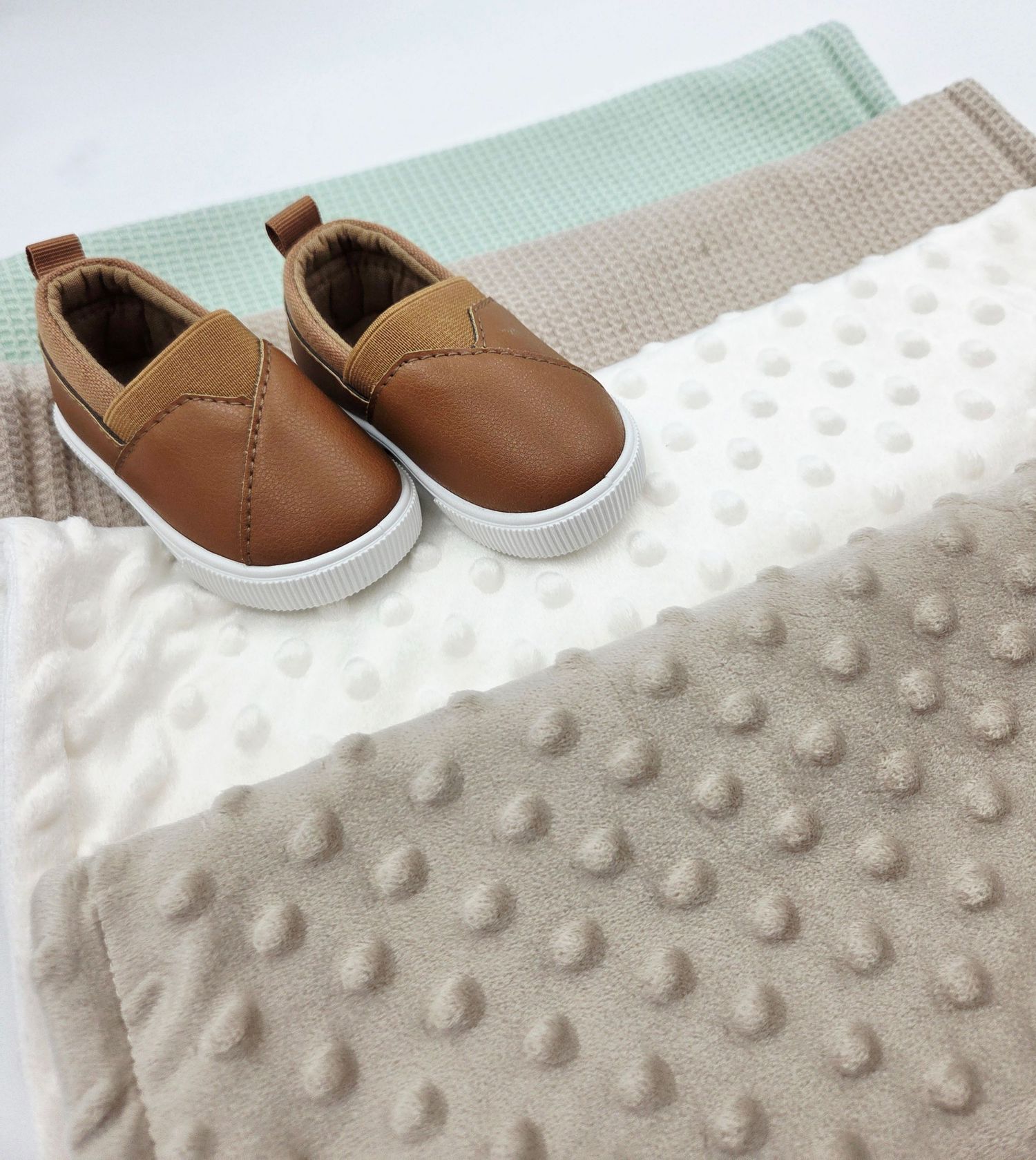 Mint green and white textured baby blanket with brown leather shoes.