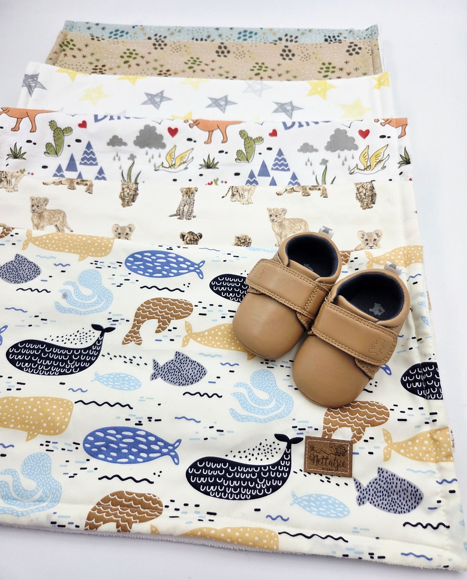 Baby moccasins displayed on whimsical patterned fabric with animal designs in blue and brown tones.