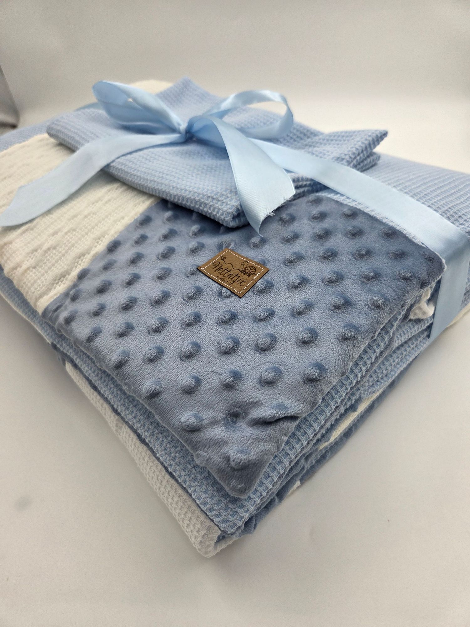 Soft blue minky dot baby blanket with white knit panel and decorative bow.