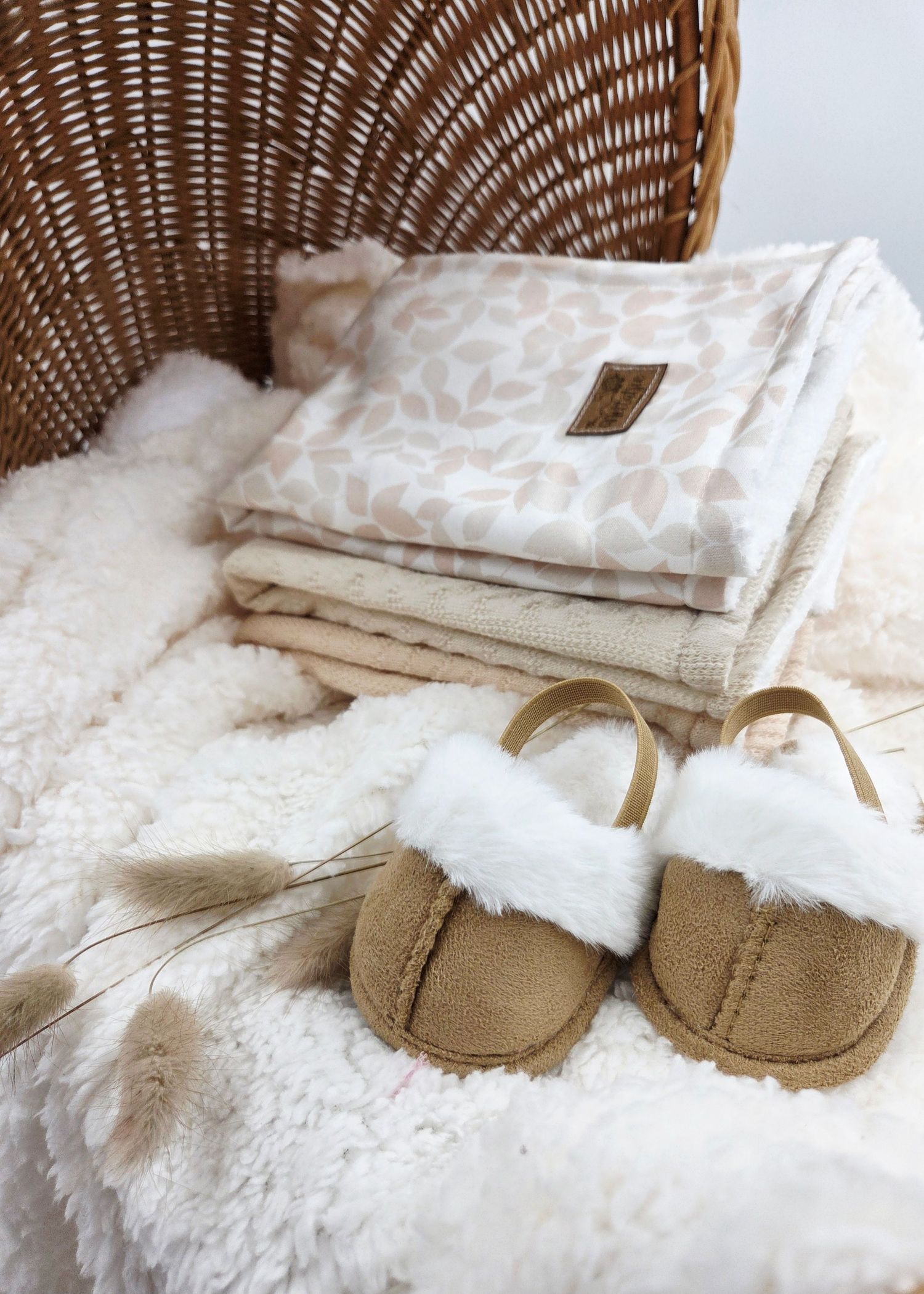 Tan baby moccasins displayed with white textured blankets in wicker basket.
