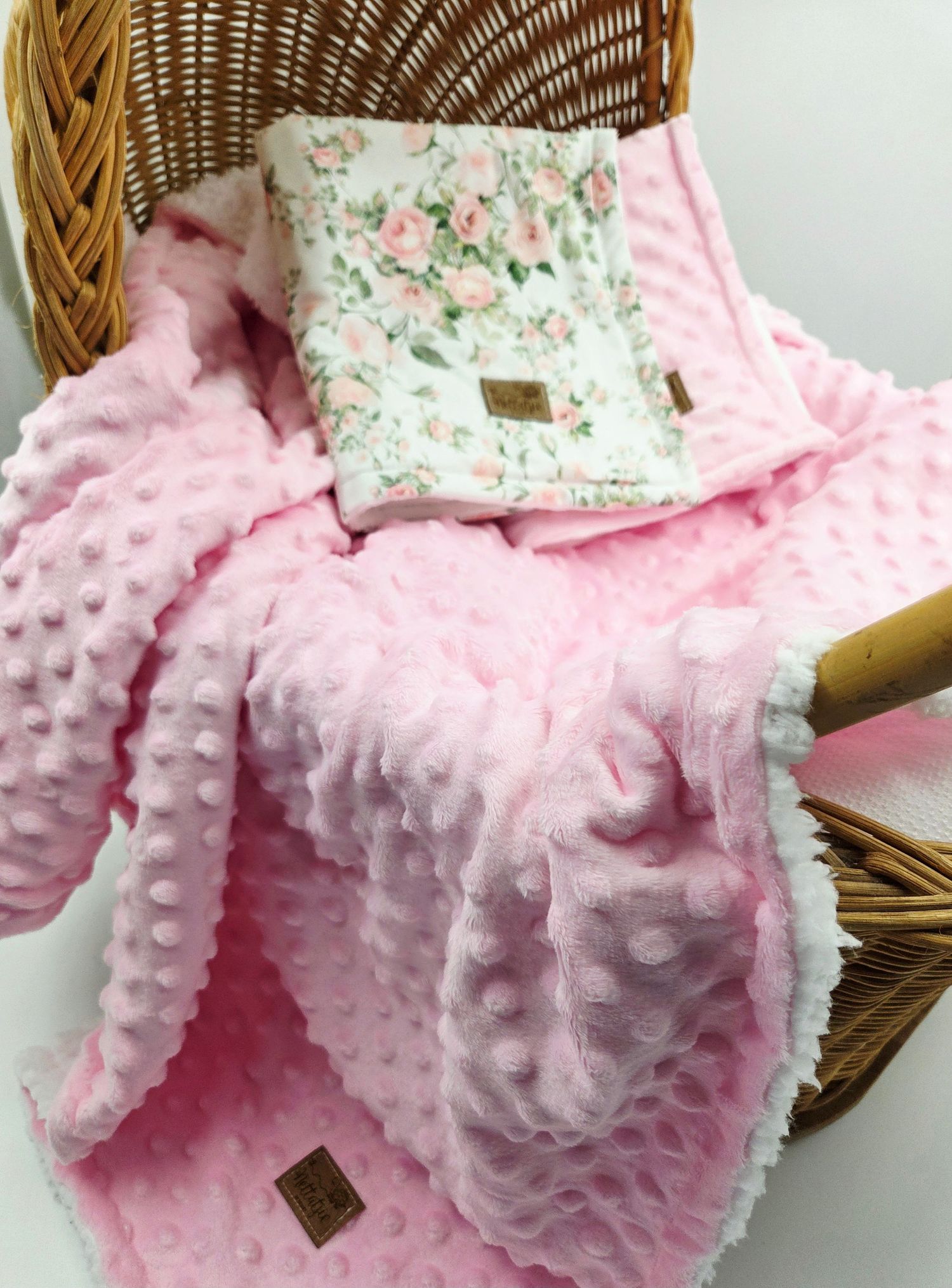 Plush pink minky baby blanket with textured dots and floral trim displayed on wicker basket.