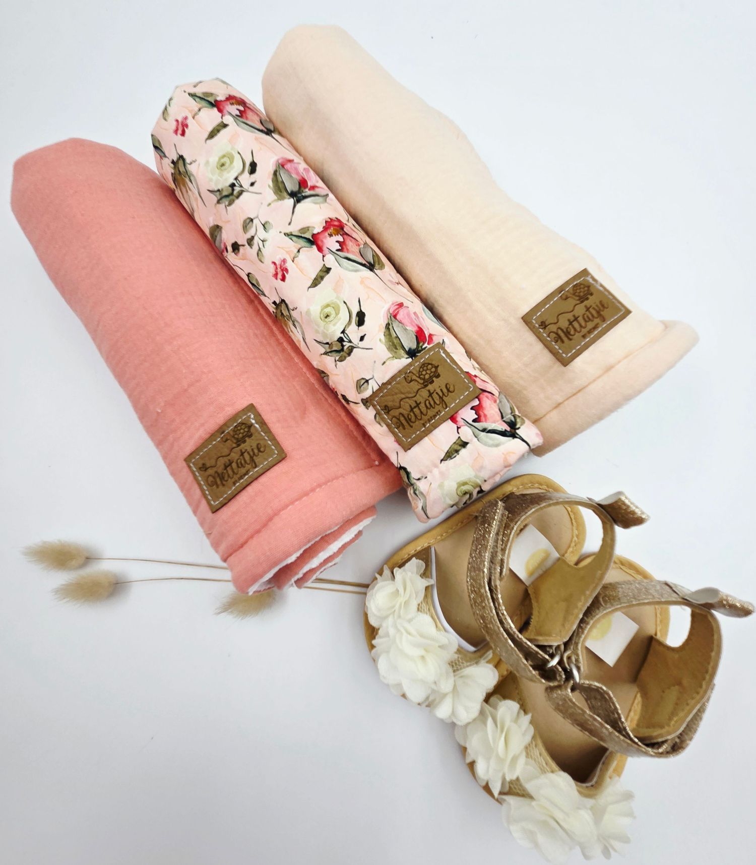 Pink and floral baby accessories with gold leather shoes displayed in elegant arrangement.
