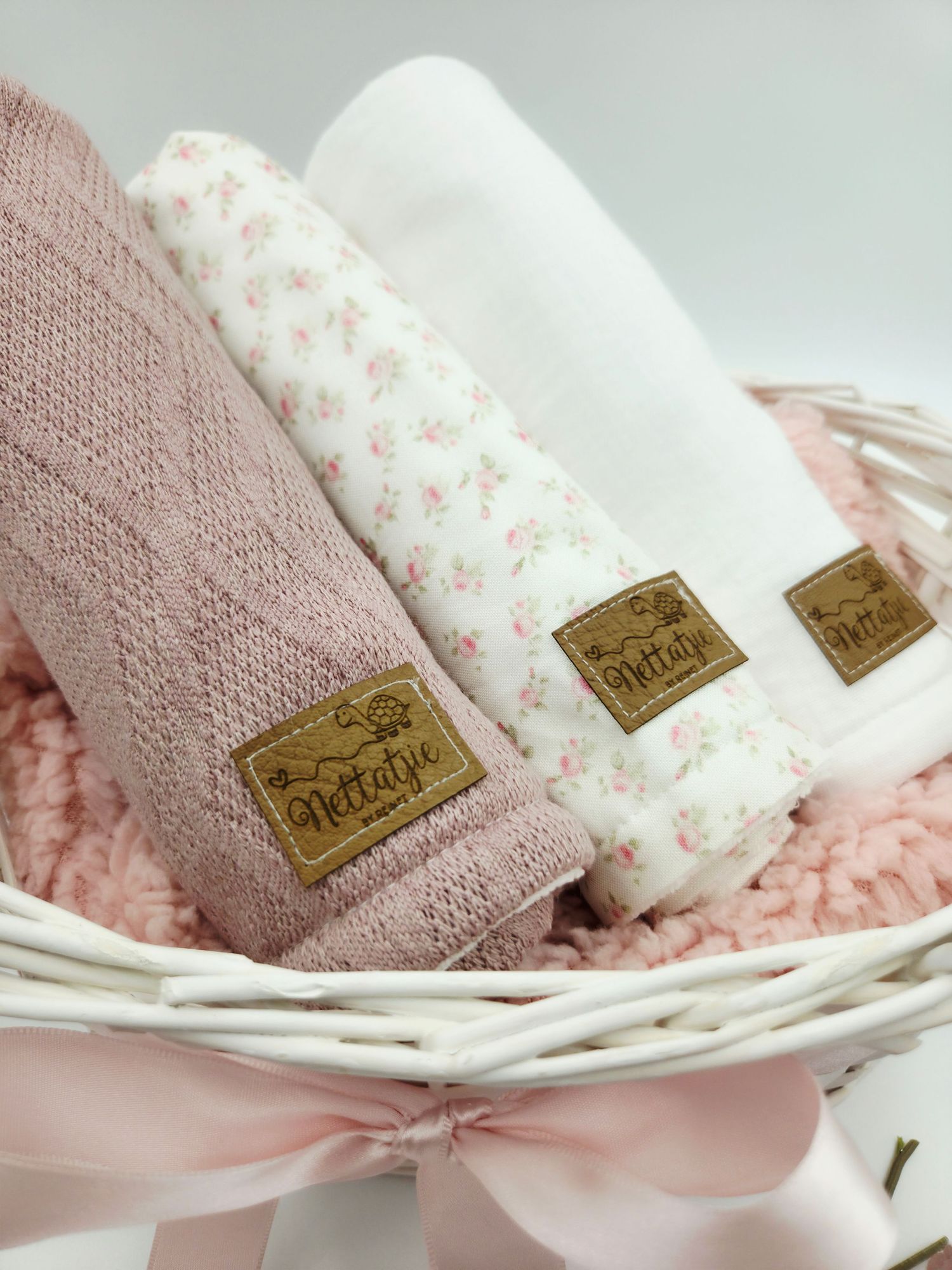 Soft pink and floral baby blankets with gold labels arranged in woven basket.