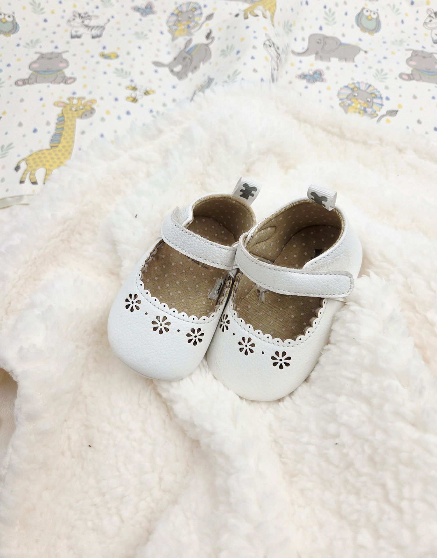 White minky baby blanket and delicate white baby shoes with floral cutout details on a light background.