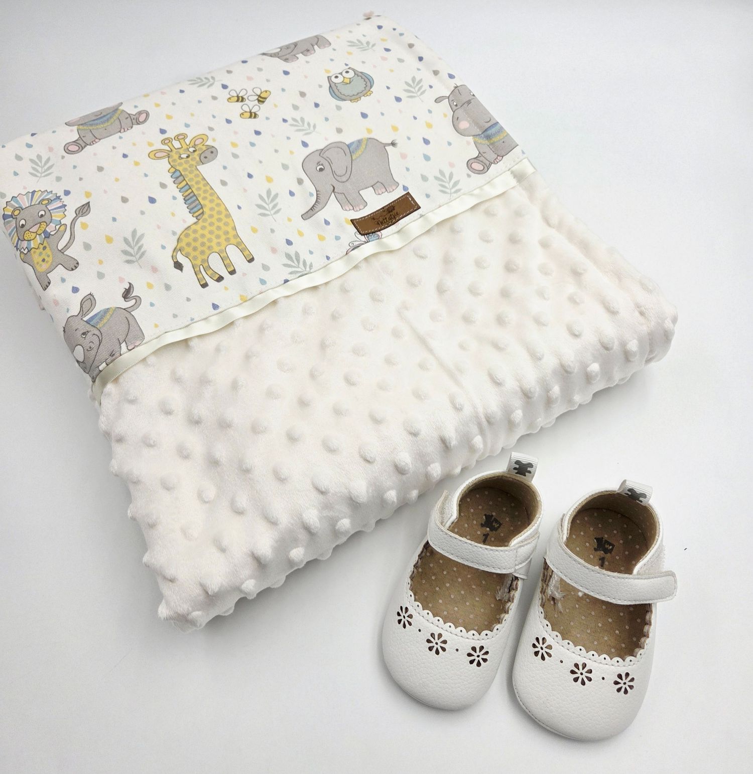 White textured minky blanket displayed with small white baby shoes in a product layout.