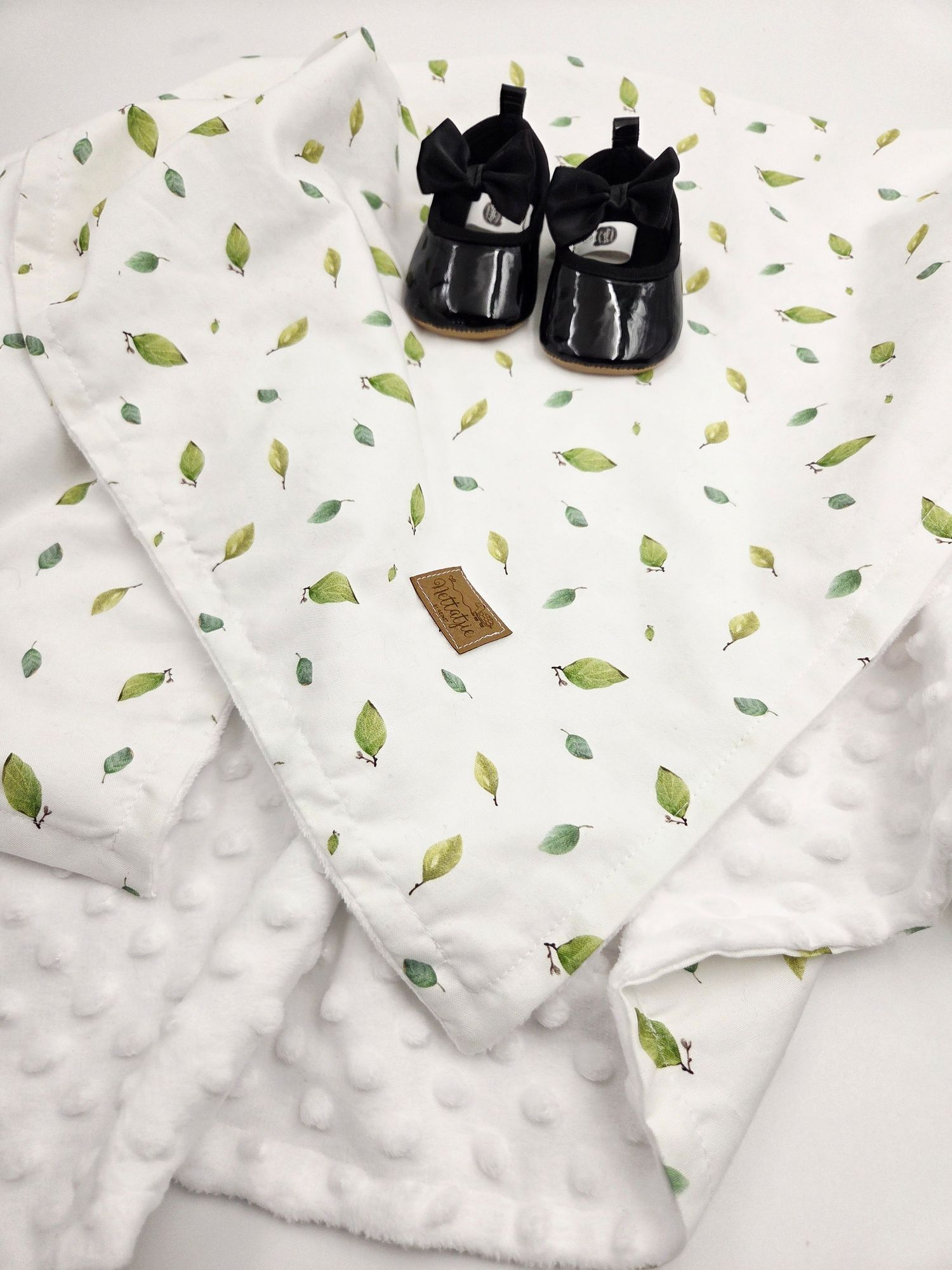 Baby blanket with leaf print pattern and minky texture shown with black baby shoes.