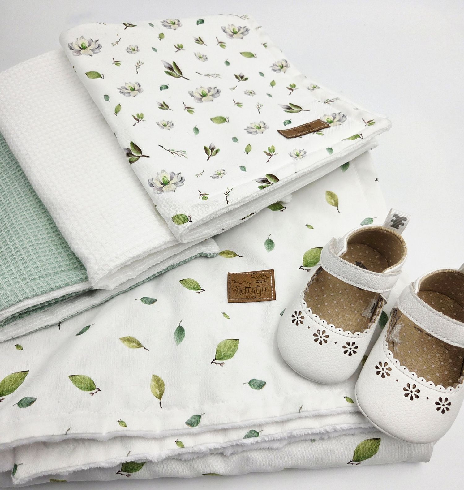 Mint green and white baby blankets with leaf pattern displayed alongside white baby shoes.