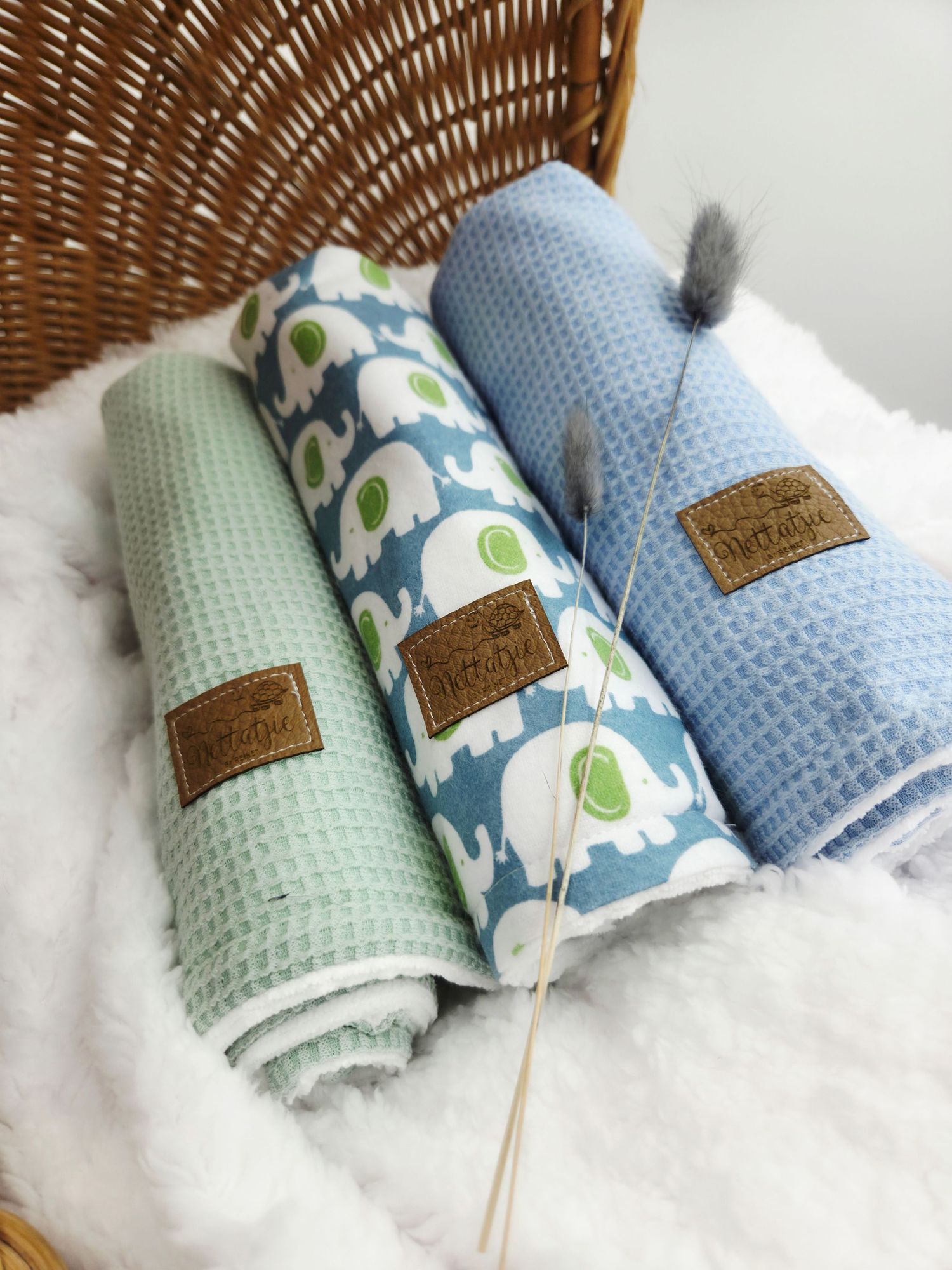 Mint green and blue patterned baby blankets arranged with brown leather labels.