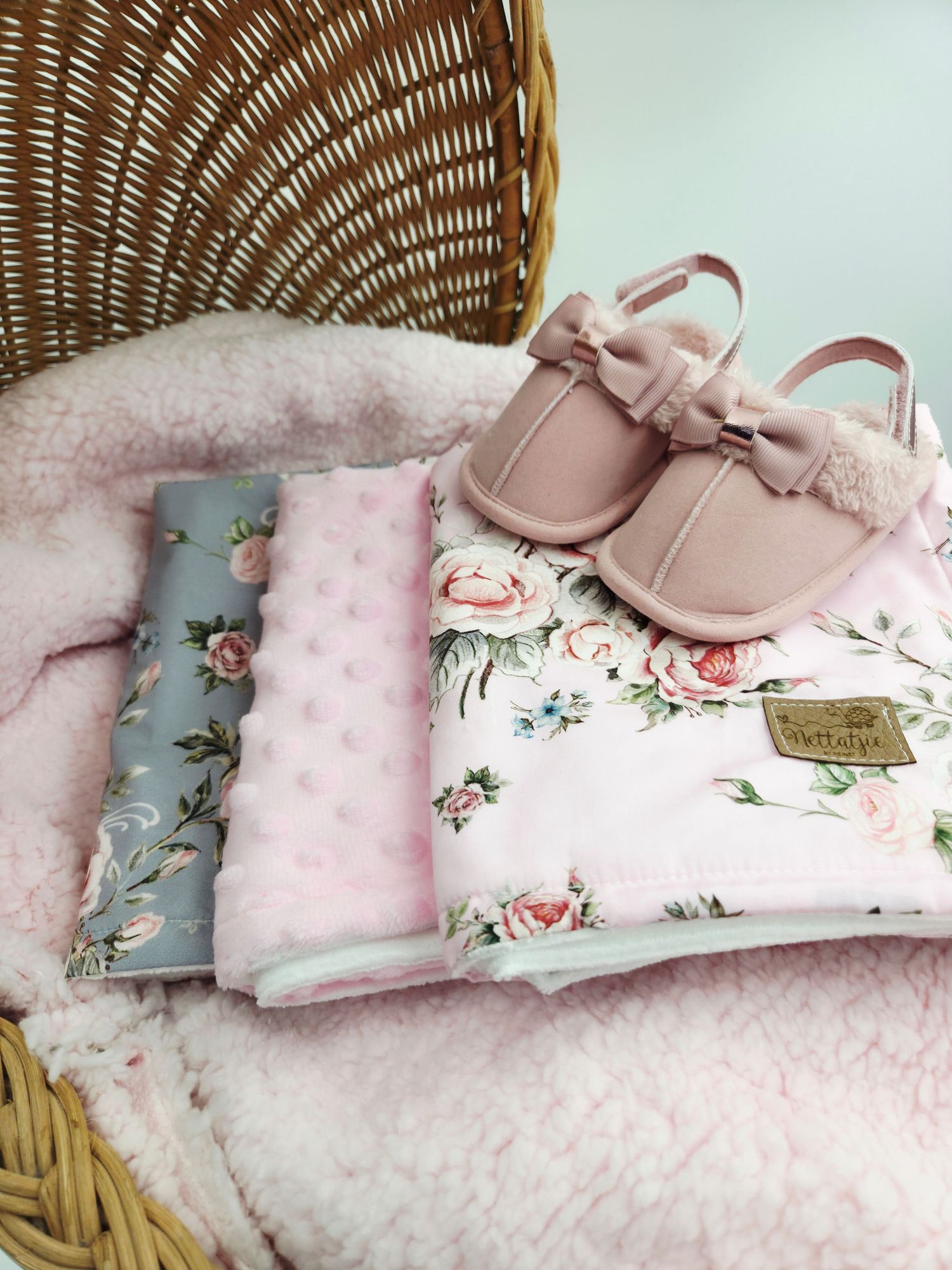 Pink and gray floral baby accessories displayed in wicker basket with soft textures.