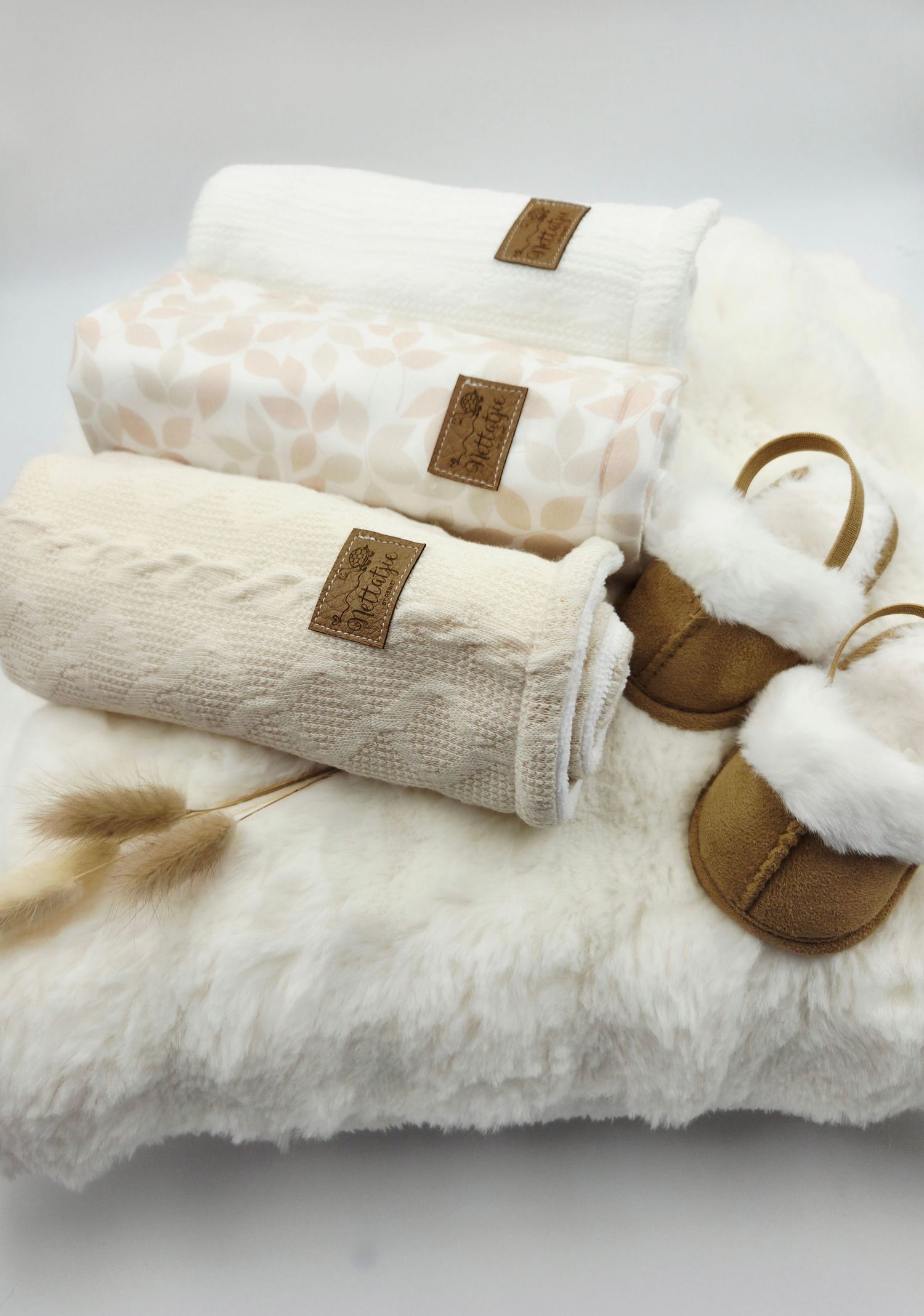 Neutral toned baby blankets and booties displayed on white furry background.