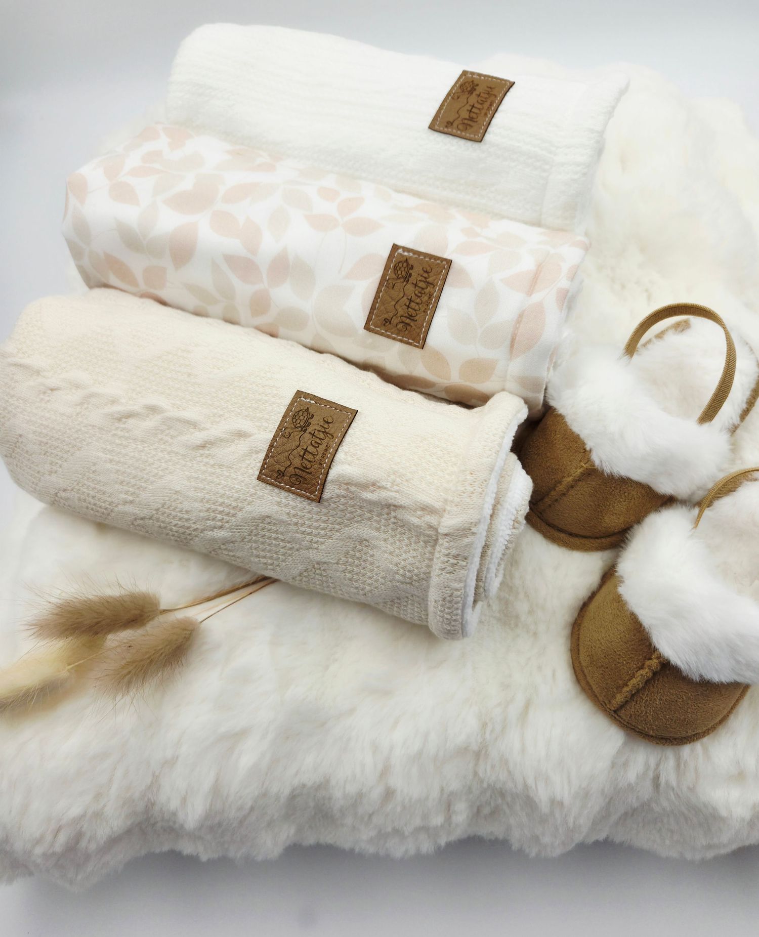 Cream colored baby blankets and brown booties arranged on white fur backdrop.