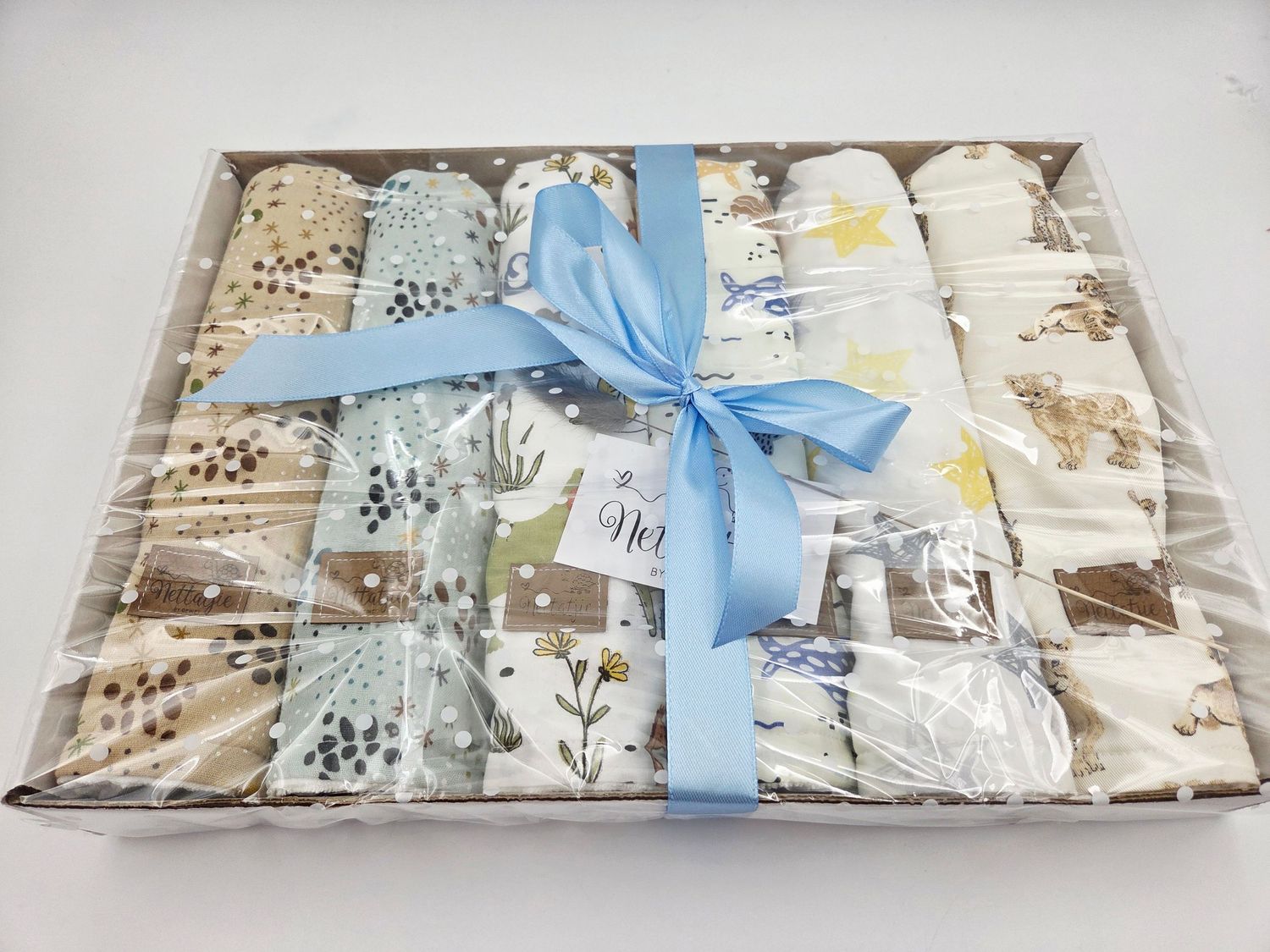Gift wrapped baby blankets with blue ribbon arranged in retail packaging display.