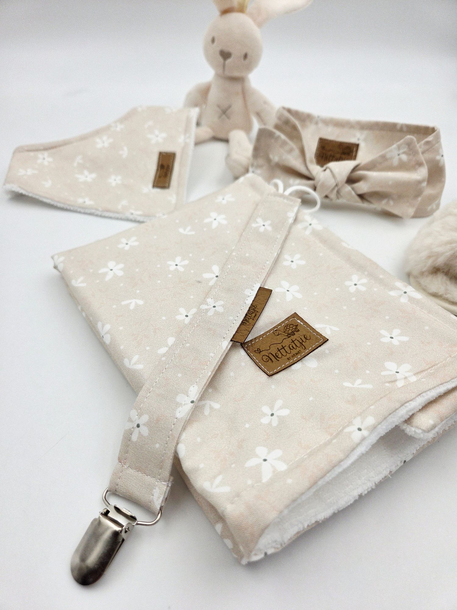 Beige security blanket with white floral pattern and plush animal attachment.