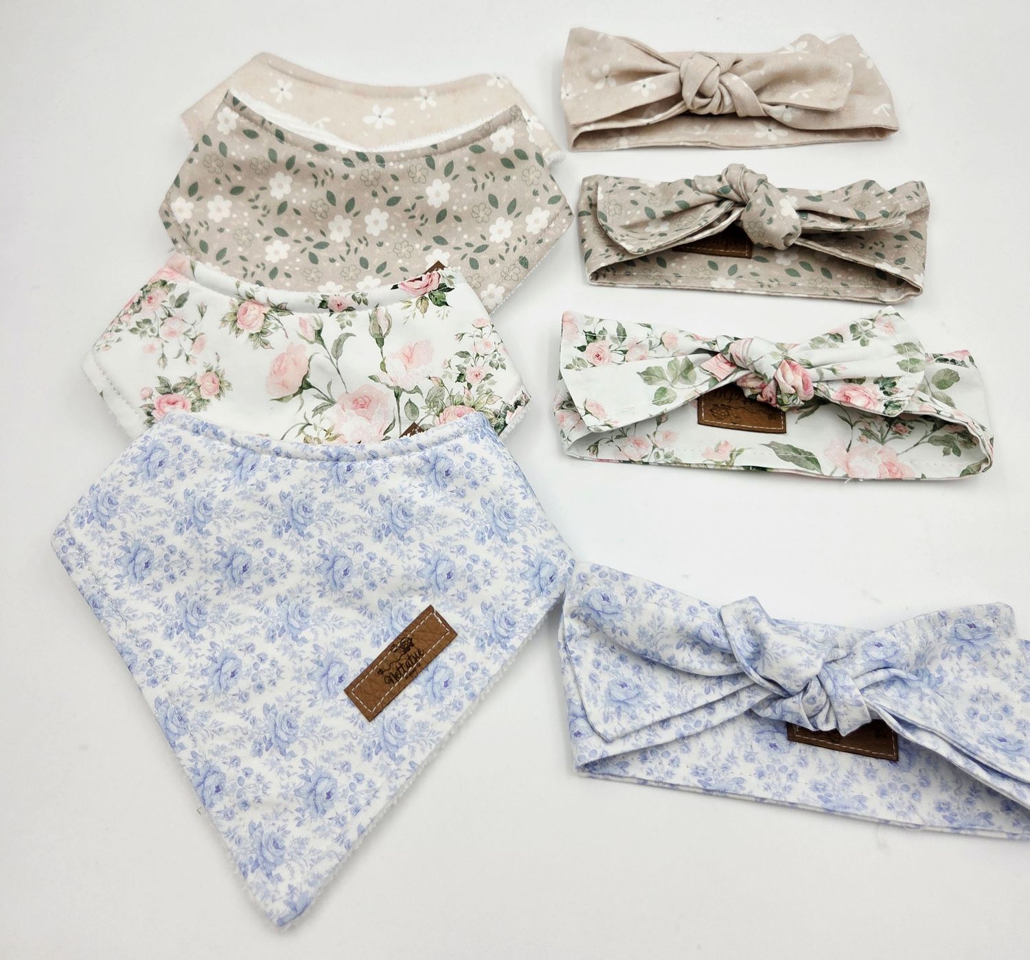 Soft floral print baby accessories including bows and bandanas in pastel blue and beige.