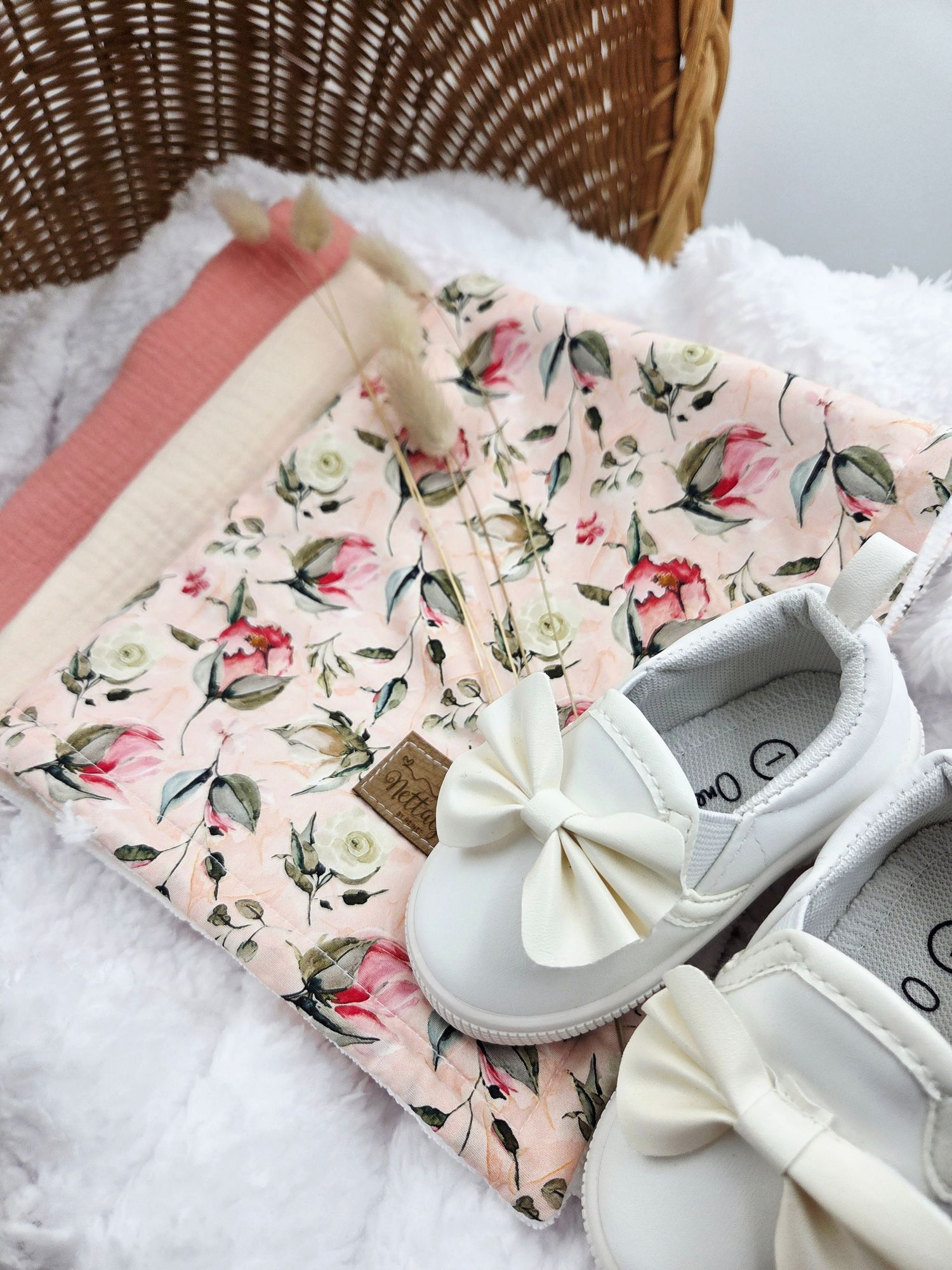 Delicate floral print baby shoes and accessories styled with wicker basket.