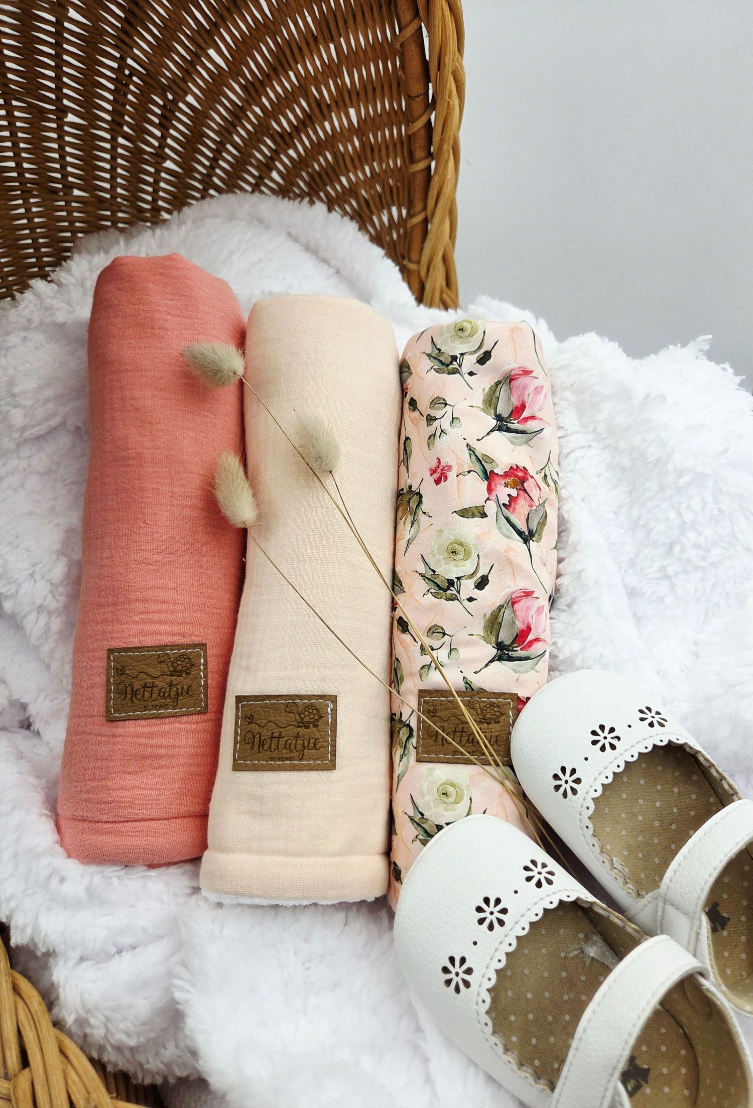 Baby accessories in coral and cream tones arranged in wicker basket with white textured fabric.