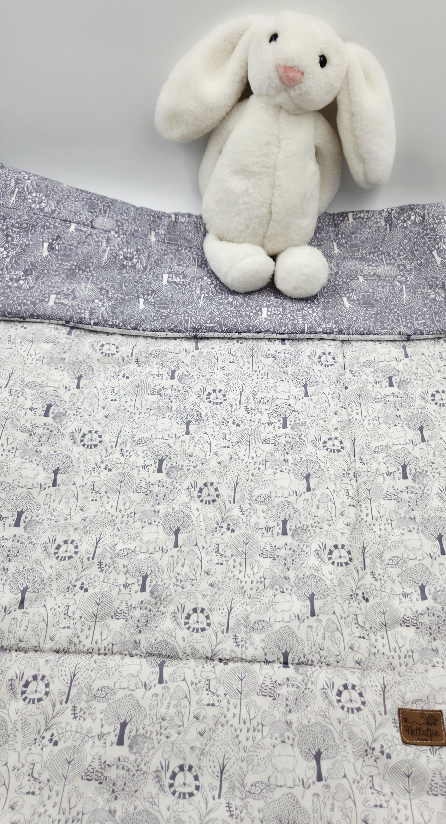 White plush bunny toy sitting on a gray and white woodland animal print baby blanket.
