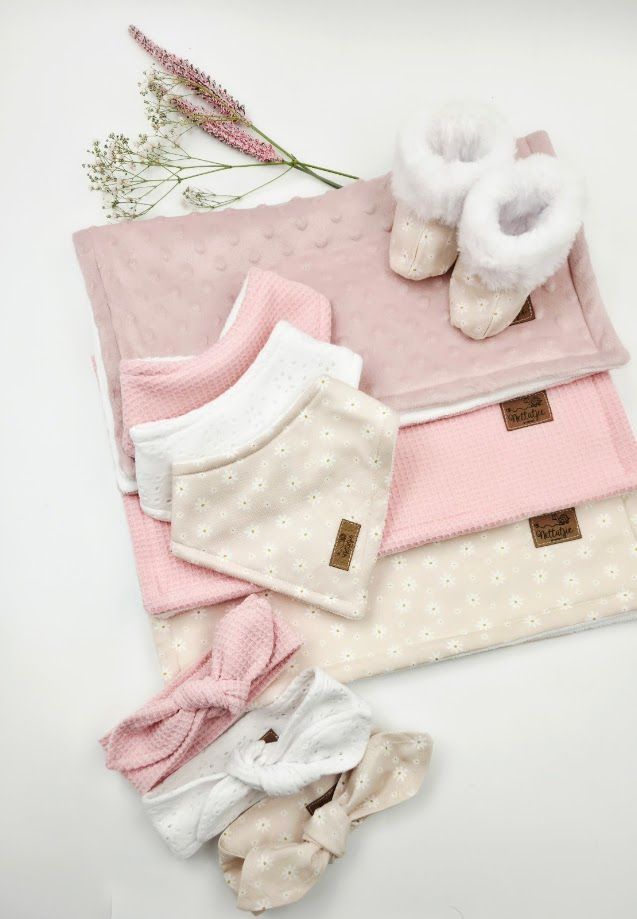 Pink baby gift set with blanket, bibs, booties, and headbands arranged on white background.
