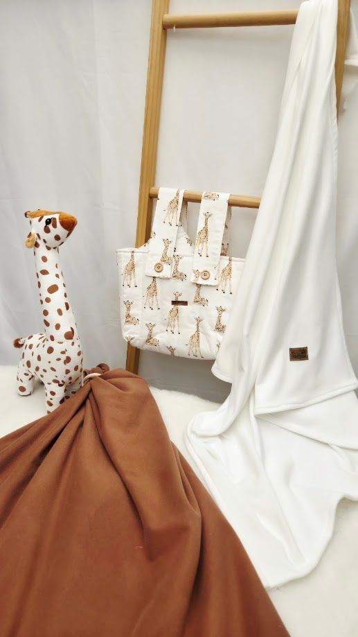 Giraffe-themed baby bag with matching blanket, brown fabric, and plush giraffe toy displayed on a wooden ladder rack.