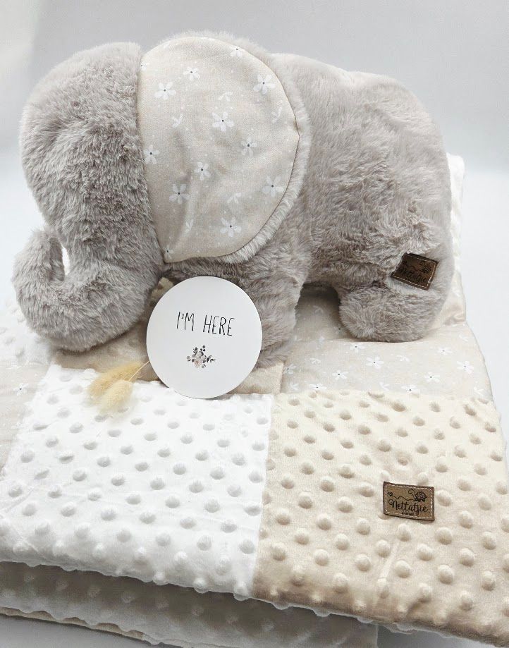 Gray plush elephant toy with star-patterned ears beside a cream minky dot baby blanket and an I'm Here milestone card.