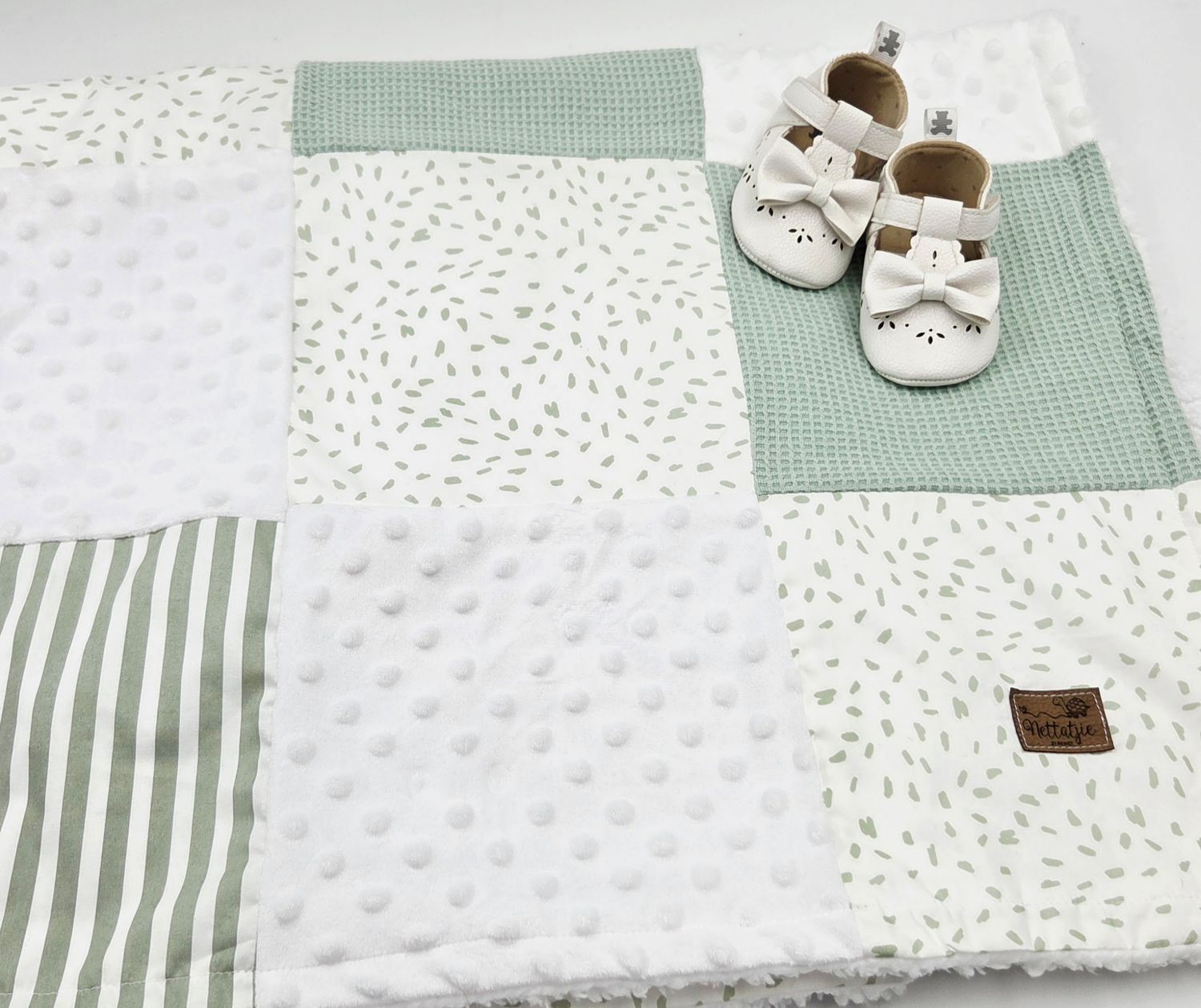 Green and white patchwork baby play mat with minky dots, stripes, and leaf prints, styled with white leather baby shoes.