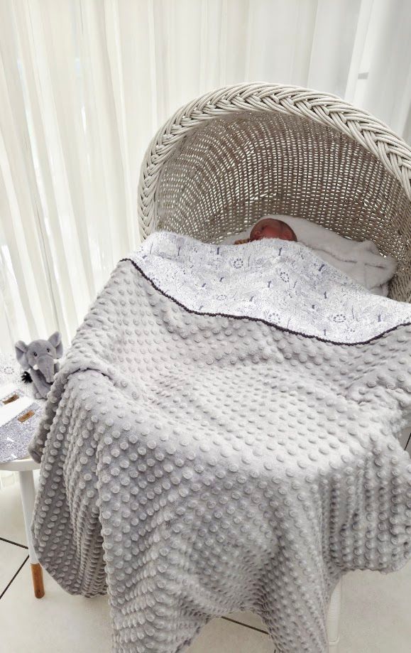 Newborn baby sleeping peacefully in a white wicker Moses basket with a soft gray bubble blanket near a bright window.