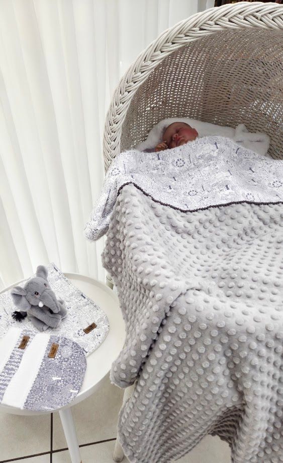 Newborn baby sleeping peacefully in a white wicker bassinet covered with a soft gray minky dot blanket.