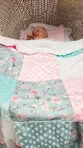 Newborn baby sleeping peacefully in a Moses basket with a colorful patchwork quilt in pink, teal, and floral patterns.