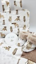 White baby gift set with leopard print wrapping paper, booties, and round keepsake box on soft blanket.