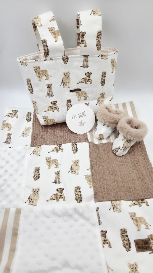 Baby gift set with wild cat print tote bag, patchwork quilt, booties, and I'm Here tag in neutral beige tones.