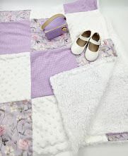 Purple and white patchwork baby quilt with floral prints, displayed with white Mary Jane shoes and a small purple bow.