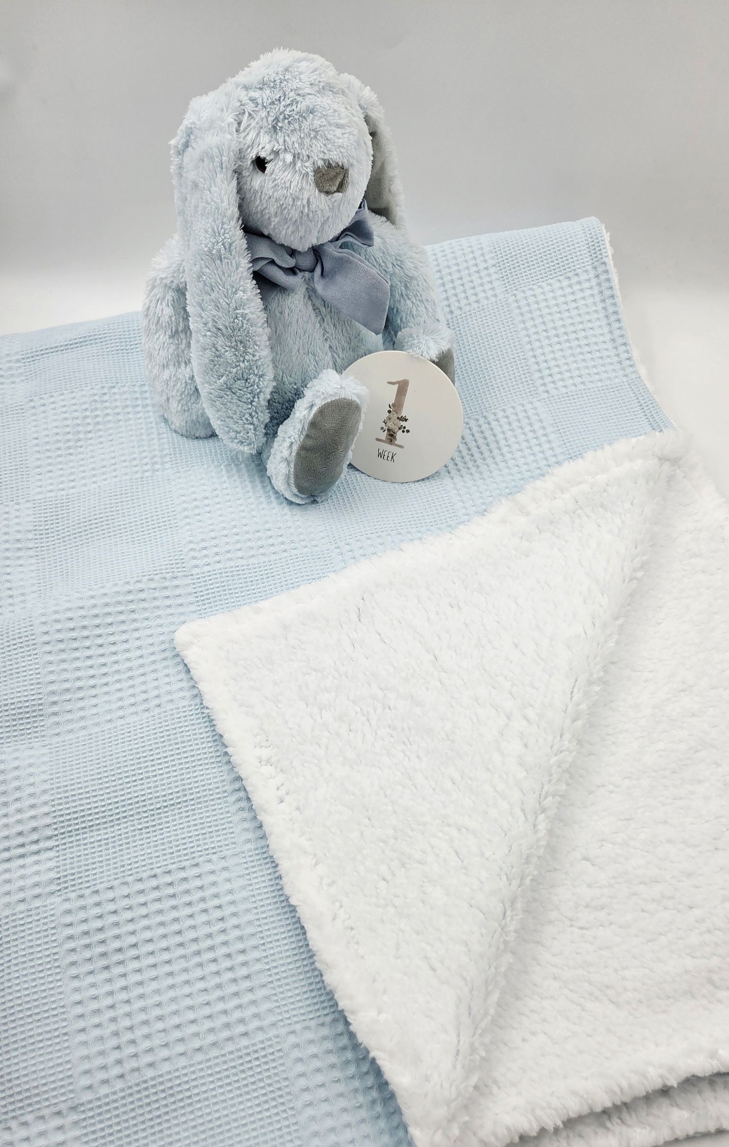 Blue waffle knit baby blanket with white sherpa lining and a soft plush blue bunny stuffed animal toy.