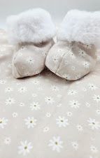 Cute white daisy print baby booties with fluffy fur trim on a matching floral fabric background.